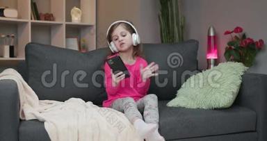 戴着<strong>蓝牙耳机</strong>的小女孩在智能手机上欣赏着mp3播放器的音乐